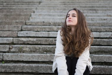 Beton s üzerinde oturan bej ceketi giyen genç güzel kadın