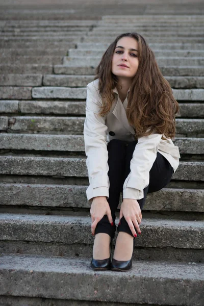 Młoda piękna kobieta noszenia kurtka beżowy, siedząc na schody betonowe — Zdjęcie stockowe