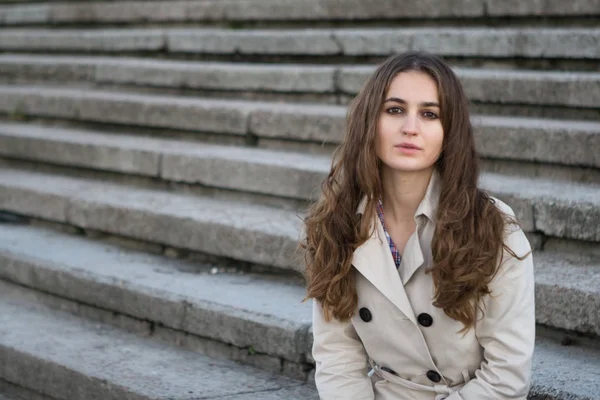 Jovem mulher bonita vestindo jaqueta bege em pé na escada de concreto — Fotografia de Stock