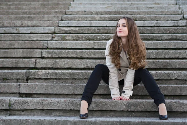 Jovem mulher bonita vestindo jaqueta bege sentado em escadas de concreto — Fotografia de Stock