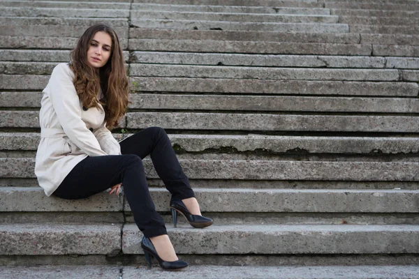 Fiatal szép nő visel bézs kabát beton lépcsőn ül — Stock Fotó