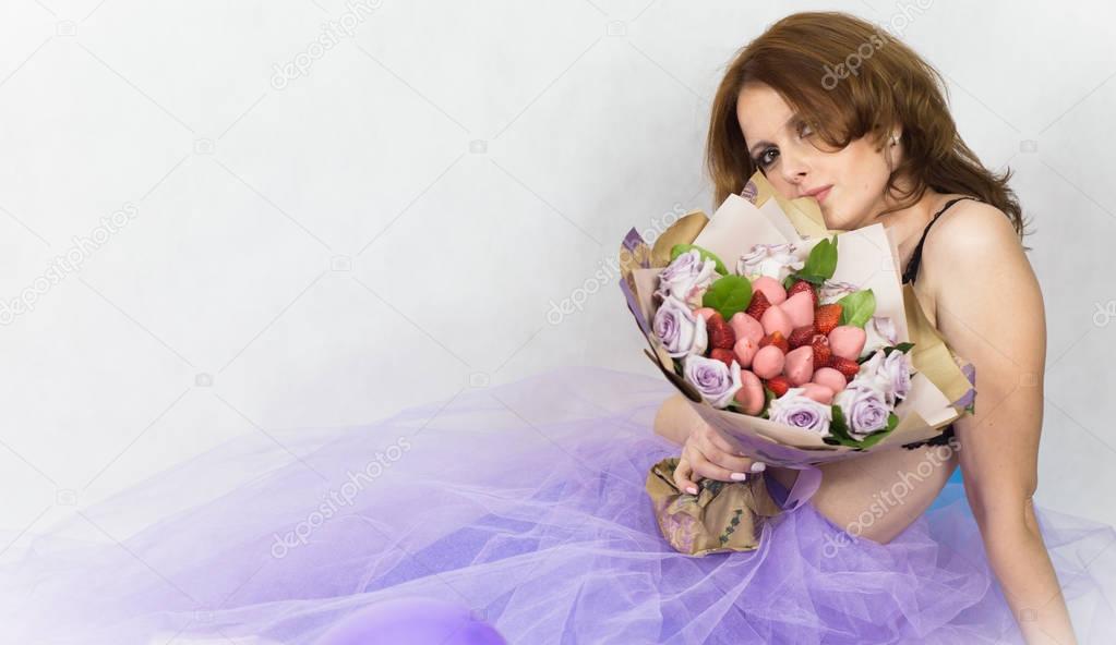 Beautiful woman in purple skirt holding bouquet from flowers, strawberry and sweets.