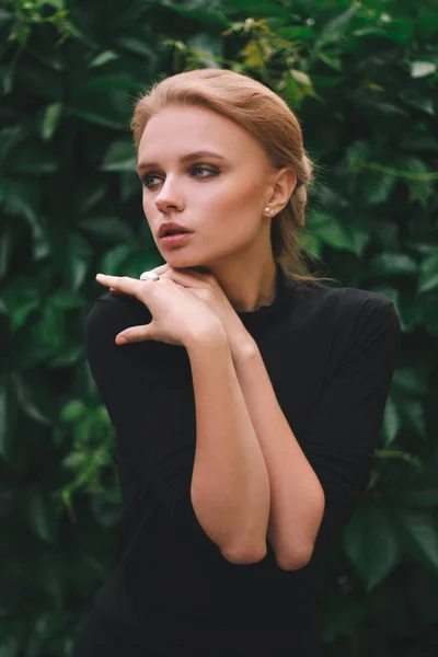 Young cute woman against background of summer green park green leaves looking at the camera — Stock Photo, Image