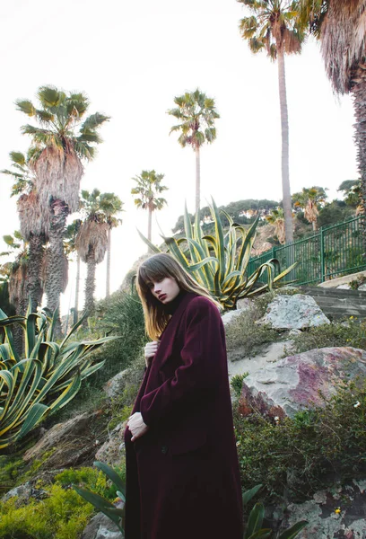 A young fashion girl in a purple coat in the mountains among the palms — Stock Photo, Image