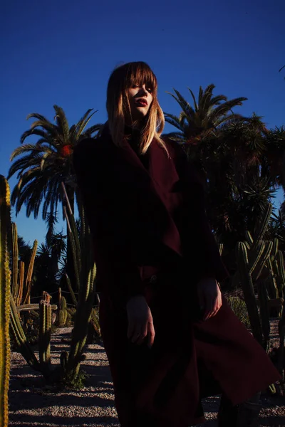 A young fashion girl in a purple coat among the palms — Stock Photo, Image