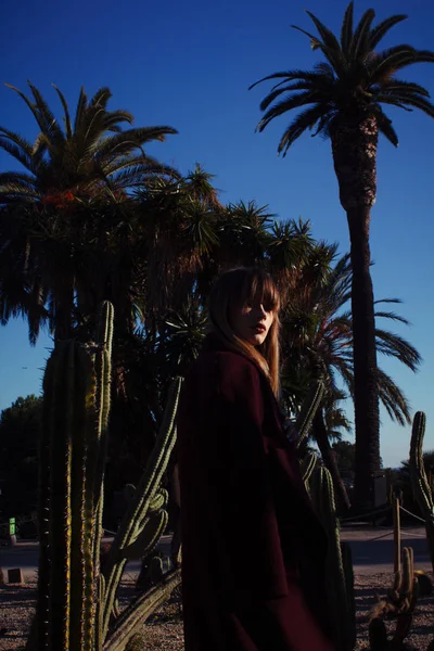 A young fashion girl in a purple coat among the palms — Stock Photo, Image