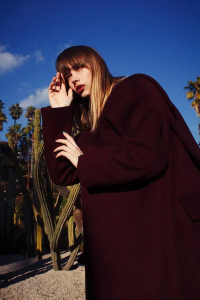 A young fashion girl in a purple coat among the palms — Stock Photo, Image