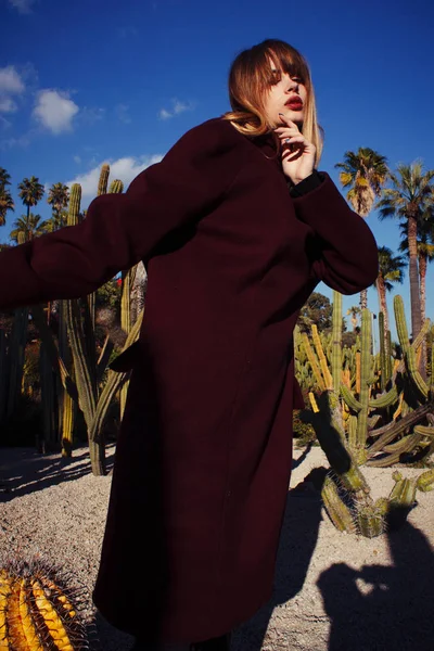 A young fashion girl in a purple coat among the palms — Stock Photo, Image