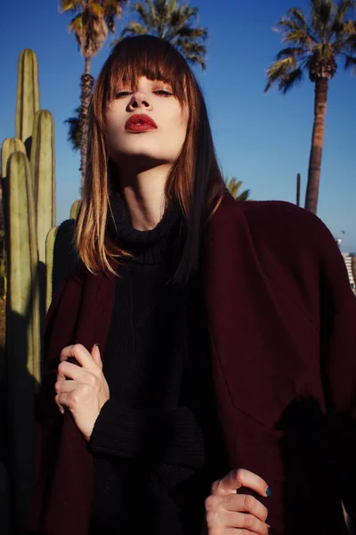 Uma jovem menina da moda em um casaco roxo entre as palmas das mãos — Fotografia de Stock
