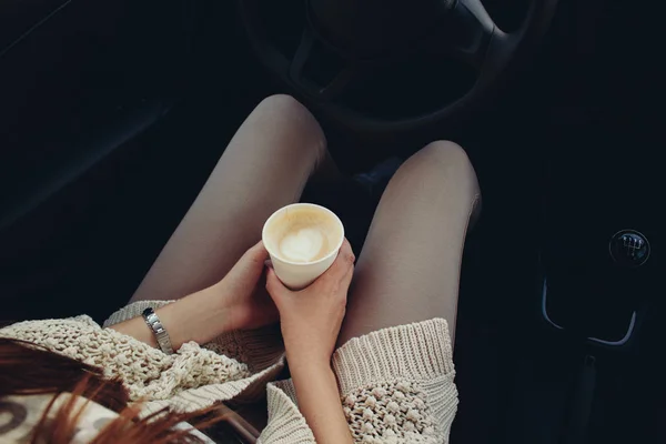 Woman sitting in a car with a paper coffee cup.