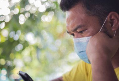 Cerrahi maske takan bir adam evde telefonla çalışıyor..