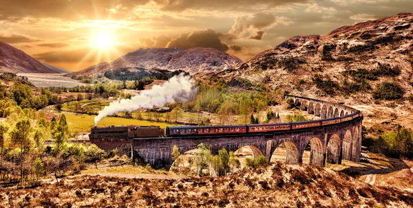 Glenfinnan Ferrocarril Viaducto en Escocia con el tren de vapor jacobita contra la puesta de sol sobre el lago —  Fotos de Stock