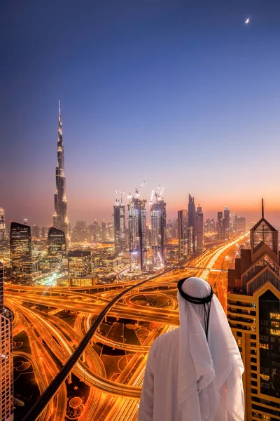 Homem árabe assistindo paisagem urbana noturna de Dubai com arquitetura futurista moderna em Emirados Árabes Unidos — Fotografia de Stock