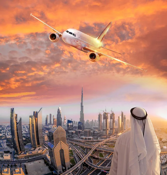 Homem árabe com avião sobrevoando Dubai contra o pôr do sol colorido em Emirados Árabes Unidos — Fotografia de Stock