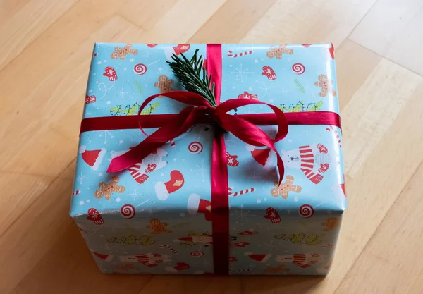 Un bonito regalo de Navidad con papel azul, símbolos de invierno y una gran cinta roja — Foto de Stock