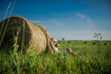 Güzel kız işten sonra dinleniyor. Sahada samanlı bir kız. Bir tarlada saman demetinin yanında bir kadın. Kırsal yaşam. Köyde tatil.