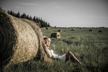 Güzel kız işten sonra dinleniyor. Sahada samanlı bir kız. Bir tarlada saman demetinin yanında bir kadın. Kırsal yaşam. Köyde tatil.