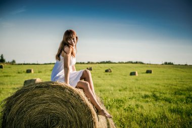 Güzel kız işten sonra dinleniyor. Sahada samanlı bir kız. Bir tarlada saman demetinin yanında bir kadın. Kırsal yaşam. Köyde tatil.