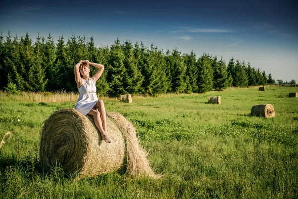 Beautiful girl is resting after work. girl on the field with hay. Woman near a sheaf of hay in a field. Rural life. Holidays in the village