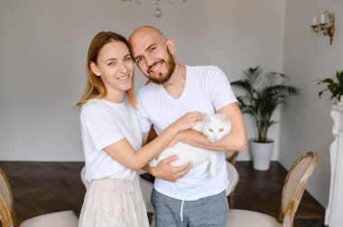 Genç bir çift kollarında beyaz bir kedi tutuyor.