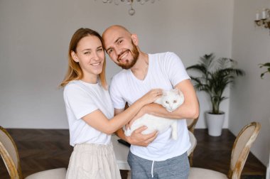 Genç bir çift kollarında beyaz bir kedi tutuyor.