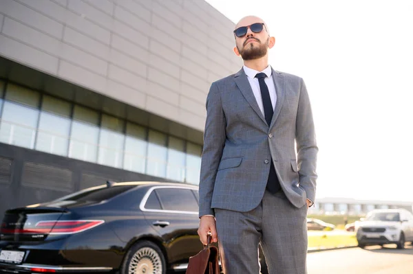 Portret van een knappe zakenman met een zonnebril in de buurt van de auto voor de moderne gevel — Stockfoto