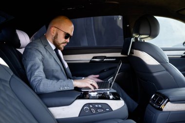 Aracın arka koltuğunda dizüstü bilgisayarı olan yakışıklı bir iş adamı. Arabayla seyahat etmek ve dizüstü bilgisayarla çalışmak.