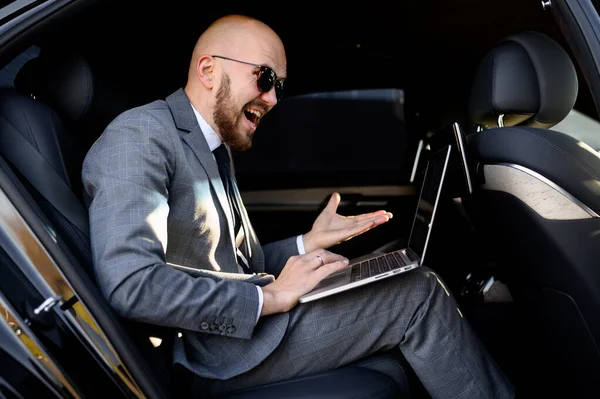 一位英俊的商人坐在车后座上，带着笔记本电脑。 乘汽车旅行，在手提电脑上工作 — 图库照片
