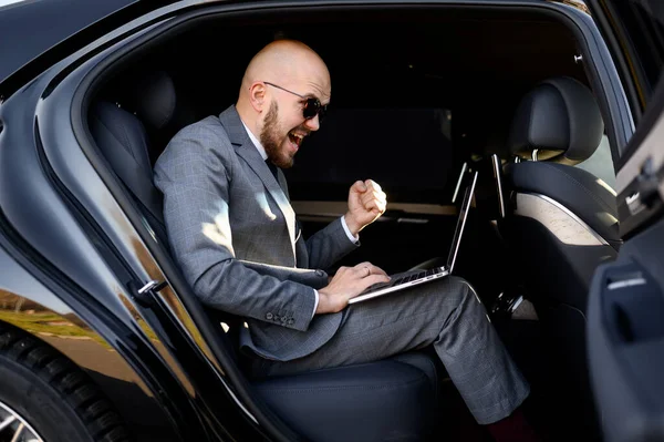 Bonito homem de negócios sentado com laptop no banco de trás do carro. viajar de carro e trabalhar no computador portátil — Fotografia de Stock