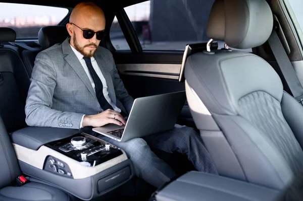 一个英俊的商人在一辆现代化的车上用他的手机，车上有一个司机在市中心。 商业、成功、旅游、奢侈品的概念 — 图库照片