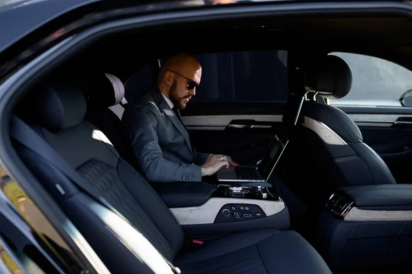 Homem de negócios trabalhando no laptop no banco de trás do carro executivo. Conceito de negócio, sucesso, viajar, luxo . — Fotografia de Stock