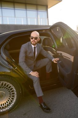 Pahalı bir arabada pahalı takım elbiseli kel bir iş adamı.