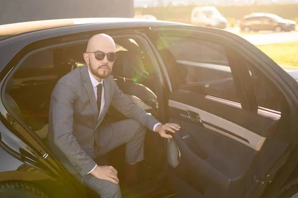 Um homem de negócios careca com barba num fato caro num carro caro — Fotografia de Stock