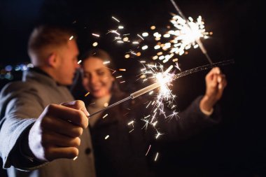 Havai fişeklerin seçici odağı açık havada tatilin tadını çıkaran genç bir çiftin ellerinde.