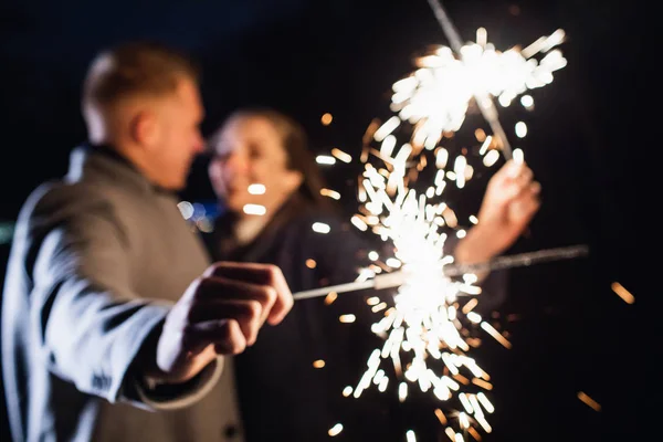 Selective focus of sparklers in hands of young couple enjoying holiday time outdoors — Stock Photo, Image