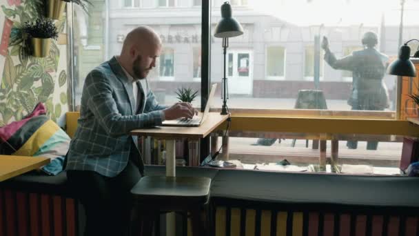 Bald man in a suit works at a laptop in a cafe — Stock Video