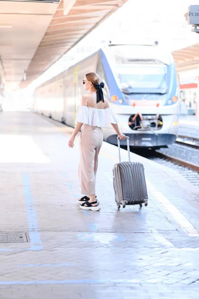 Lány napszemüveg a vasútállomáson egy bőrönt a háttérben a vonat — Stock Fotó