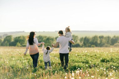 Mutlu genç aile dışarıda yeşil doğada birlikte vakit geçiriyor.