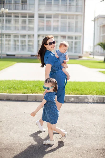 Młoda matka z córkami ubranymi w dżinsowe sukienki. Rodzinne spojrzenie. Szczęśliwa rodzina — Zdjęcie stockowe
