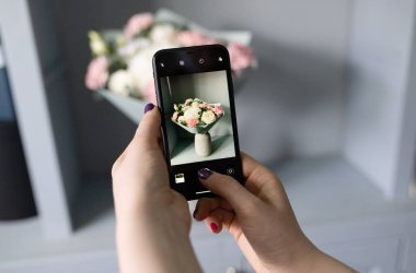 Kız blogcu telefonuyla çiçeklerin fotoğrafını çekiyor.