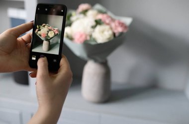 Kız blogcu telefonuyla çiçeklerin fotoğrafını çekiyor.