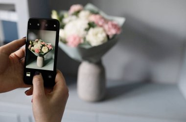 Kız blogcu telefonuyla çiçeklerin fotoğrafını çekiyor.