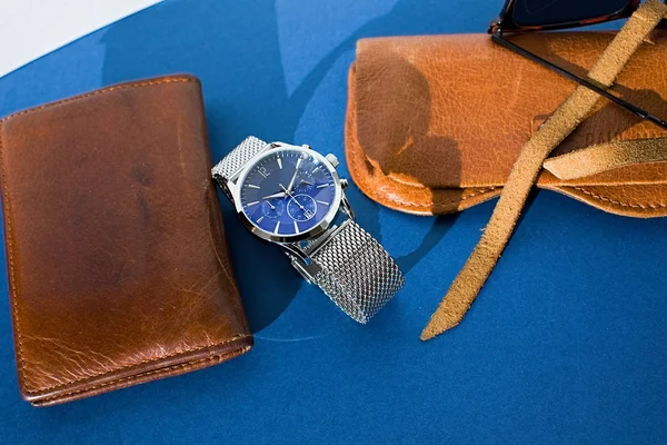 Portamonete in pelle, orologio con bracciale in metallo, occhiali da sole e laptop su sfondo blu. Accessori per uomo. Vista dall'alto — Foto Stock