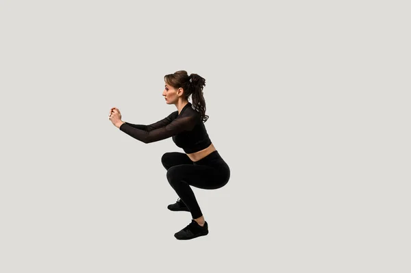 Full length portrait of a young fitness woman doing squatting isolated on a white background — 스톡 사진