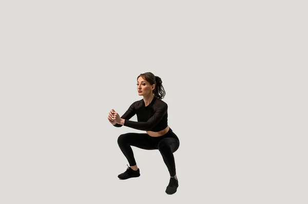 Full length portrait of a young fitness woman doing squatting isolated on a white background — 스톡 사진