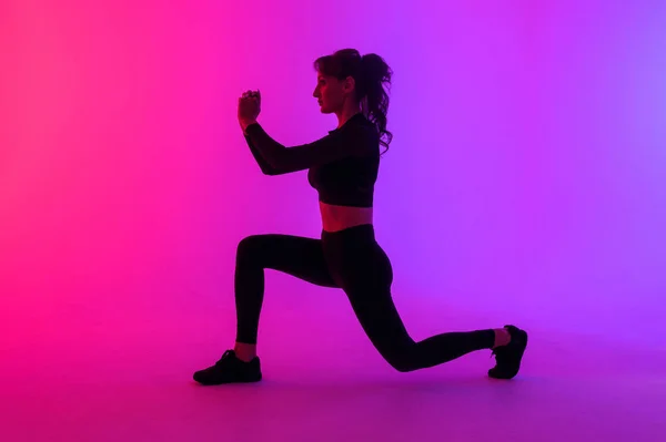 Retrato de larga duración de una joven fitness haciendo sentadilla aislada sobre un fondo de colores vibrantes — Foto de Stock