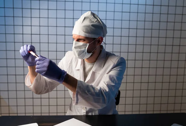 Χέρια ενός τεχνικού εργαστηρίου με ένα σωλήνα δείγματος αίματος και μια σχάρα με άλλα δείγματα. τεχνικός εργαστηρίου που κρατά δείγμα σωλήνα αίματος για μελέτη — Φωτογραφία Αρχείου
