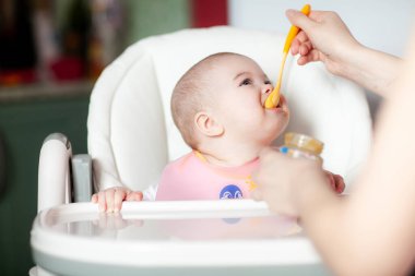 Anne bebeğini kaşıkla besliyor. Bebek yemek.