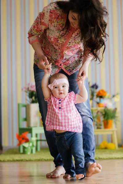 Concepto de familia, infancia y paternidad: un bebé feliz aprendiendo a caminar con la ayuda de la madre en casa —  Fotos de Stock