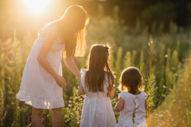 Aile gün batımında doğada yürüyor. Annenden iki çocuk.